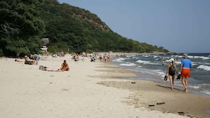 A beach with people sunbathing and walking along the shore. - Stenrosgården logi (Kivik)