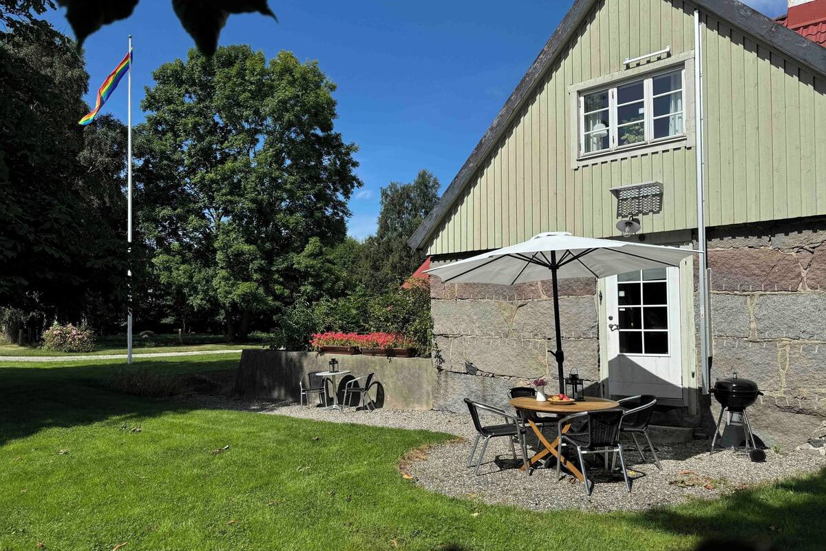 En bygning med en stenfassade, et flagstang og en patio med udendørs møbler.