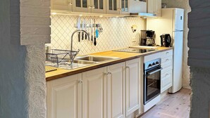 A kitchen with white cabinets, a wooden countertop, a sink, a stove, and a hanging light fixture. - Stenrosgården logi (Kivik)