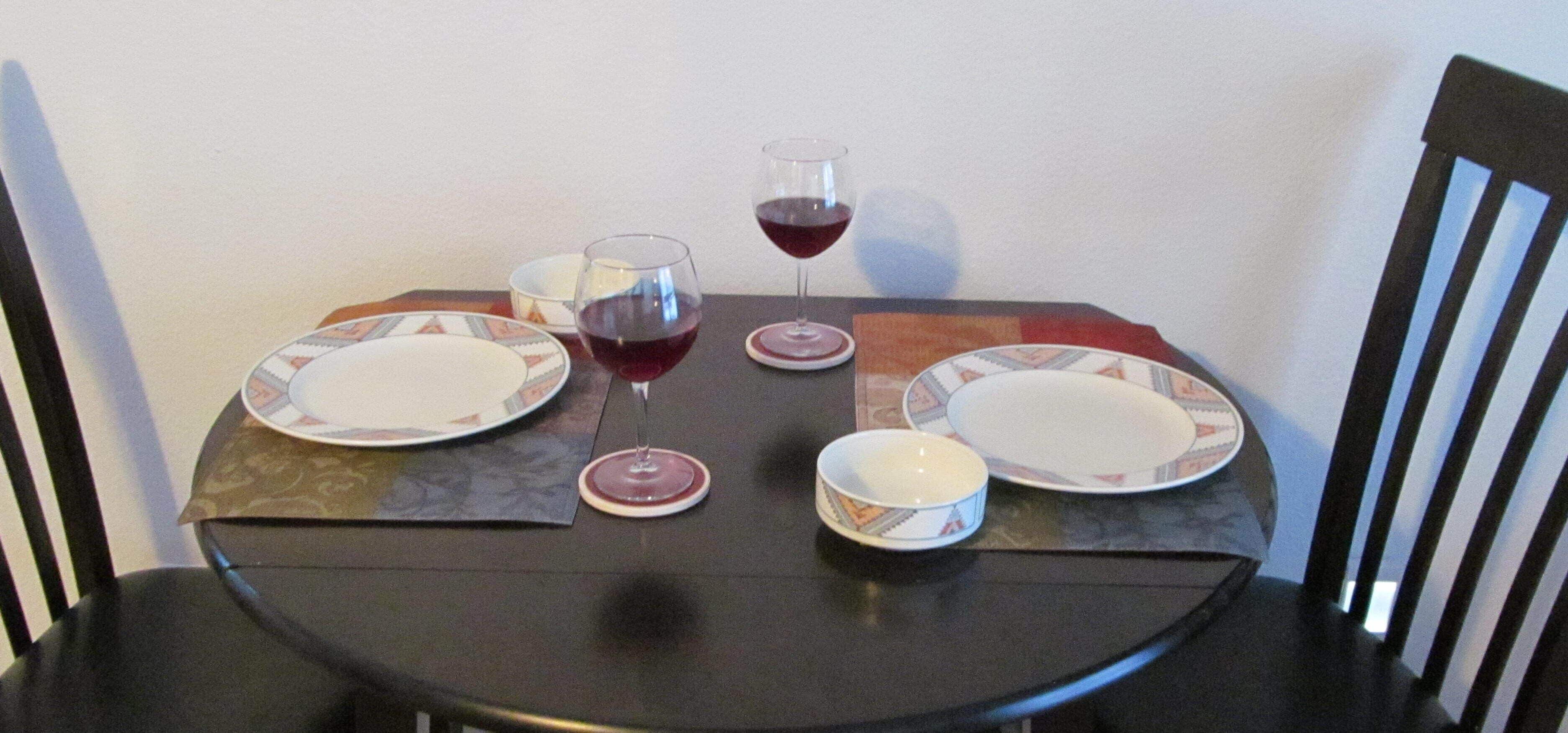 Una mesa de comedor dispuesta con platos, tazones y copas de vino.