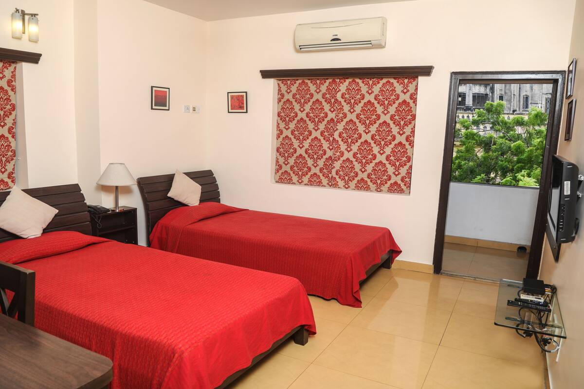 A hotel room with two beds, a TV, an air conditioner, and a balcony with a view.