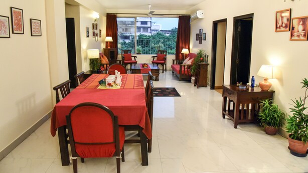 Un coin repas avec une table et des chaises rouges, un ventilateur de plafond et une vue sur les bâtiments à travers une grande fenêtre.