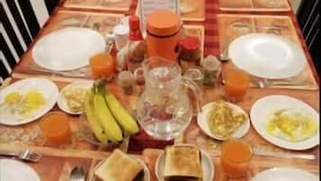 Una mesa de comedor preparada con cosas para el desayuno, como platos, tostadas, plátanos y zumo de naranja.