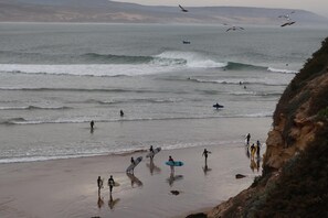 A beach with surfers and a boat in the water. - Azul Guest House Taghazout Bay - Hostel (Aourir)