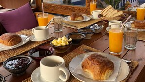 A breakfast table with croissants, fruit, coffee, and juice, set against a view of a desert landscape.