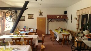 A dining area with multiple tables set for meals, wooden chairs, and a large wooden wheel structure.