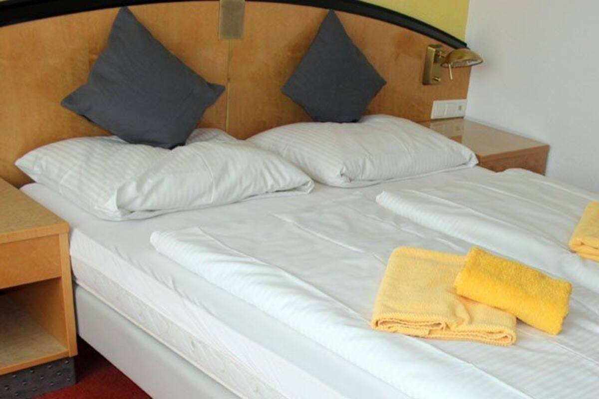 Ein ordentlich gemachtes Bett mit weißen Leinentüchern und zwei gefalteten gelben Handtüchern.