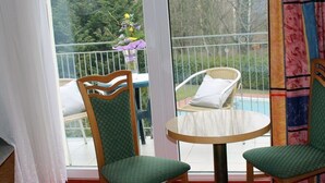 A balcony with two chairs and a table, a view of a swimming pool, and a window with curtains.