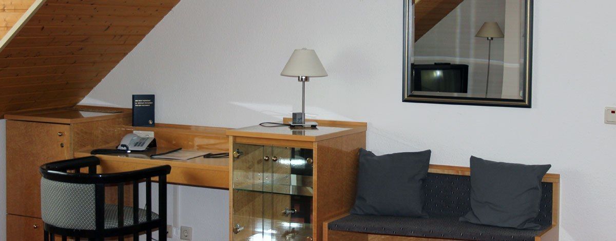 A compact room with a wooden desk, a chair, a sofa with cushions, a lamp, and a mirror on the wall.