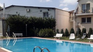 A swimming pool with steps leading into it, surrounded by benches and a building with balconies.