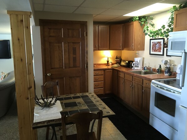 A compact kitchen with wooden cabinets, a dining table with chairs, a coffee maker, and a microwave. - The Perfect Place to "GETAWAY' (Big Bay)