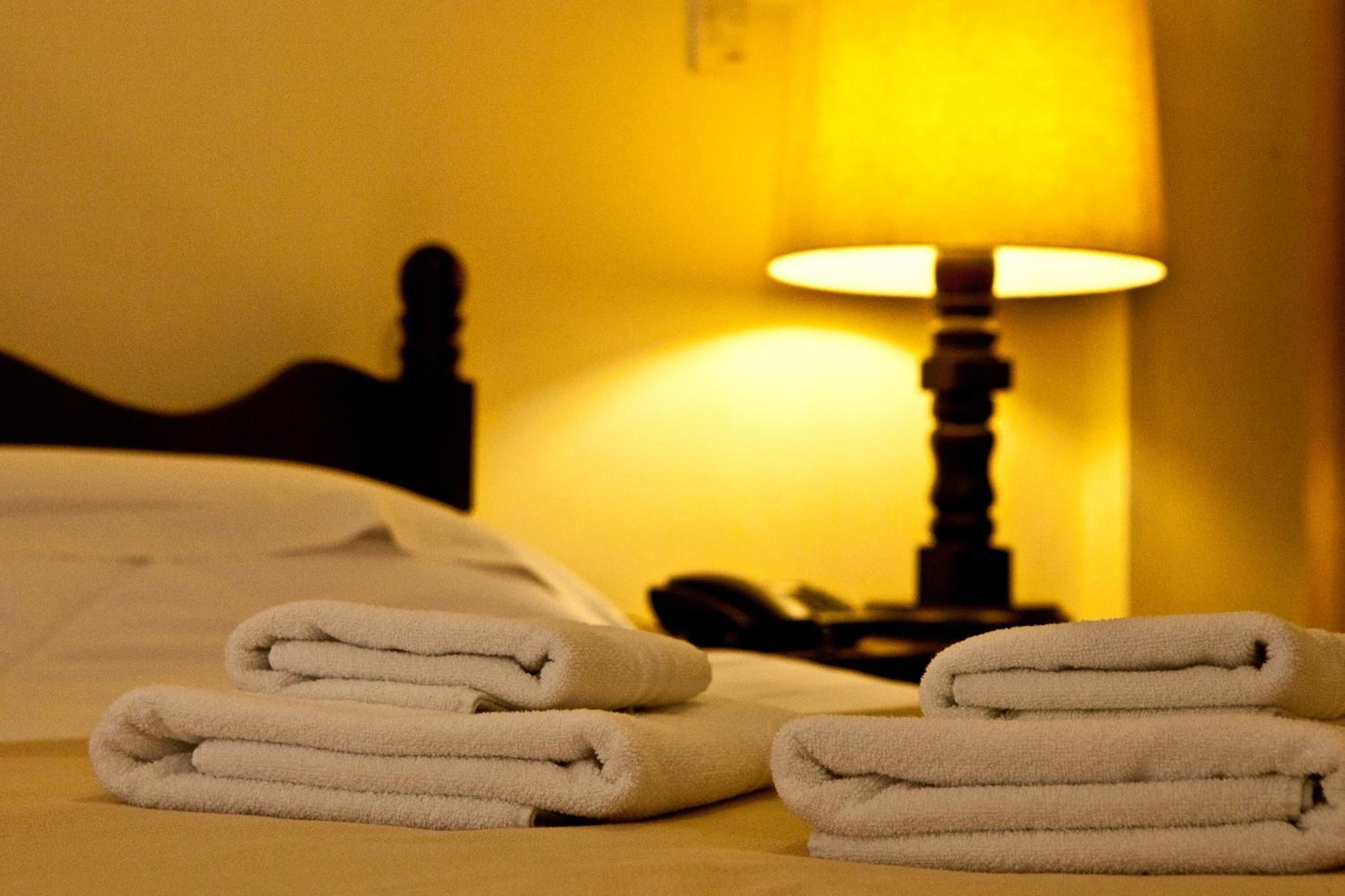 Ein ordentlich bezogenes Bett mit gefalteten weißen Handtüchern und einer Lampe im Hintergrund.