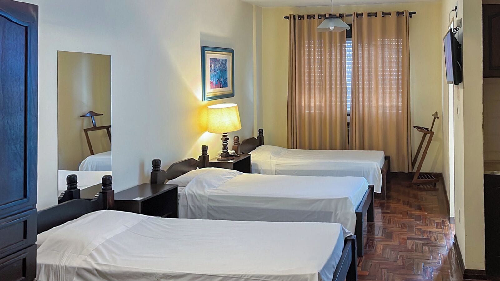 A hotel room with two beds, a desk, a chair, a lamp, a picture on the wall, and a TV mounted on the wall.