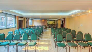Un salón de conferencias con filas de sillas verdes, una mesa de recepción y vistas a través de un muro de cristal.