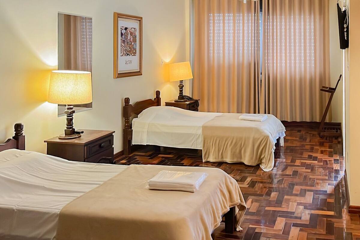 A hotel room with two beds, a wooden floor, a window with curtains, and a framed picture on the wall.