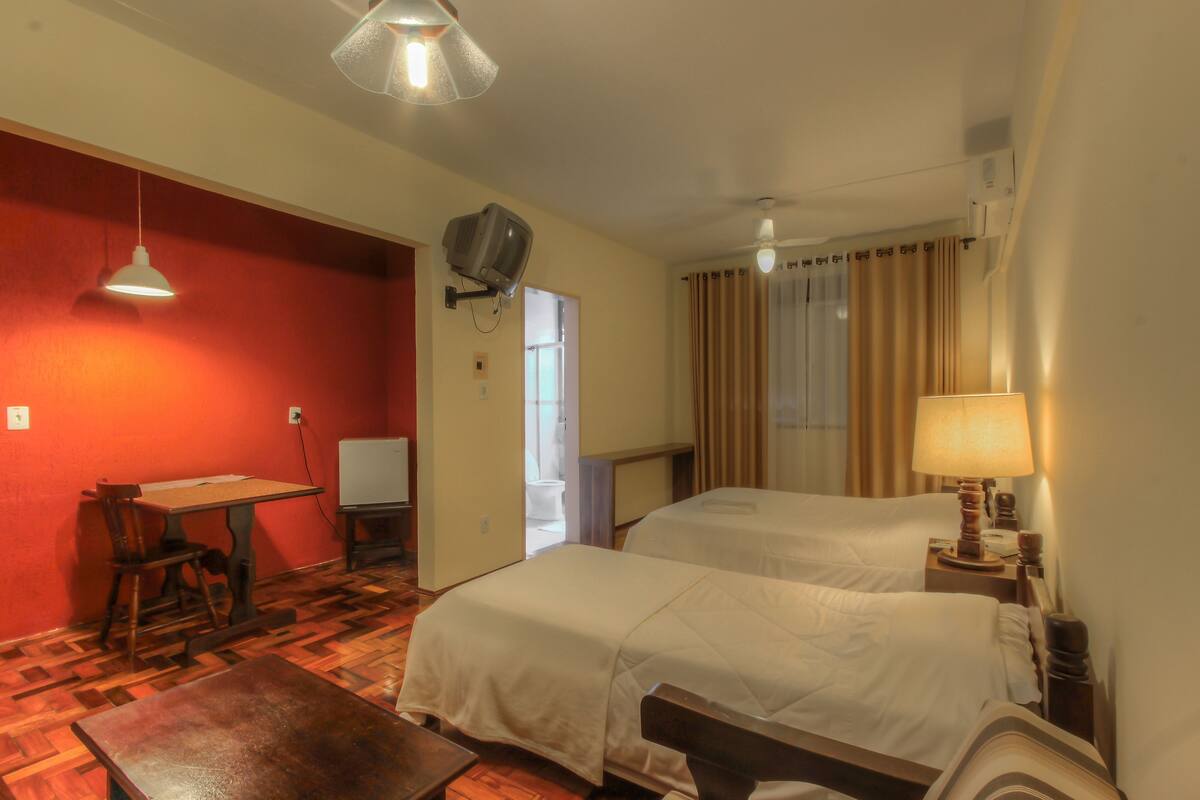 A hotel room with two beds, a desk, a chair, a television, and a lamp.