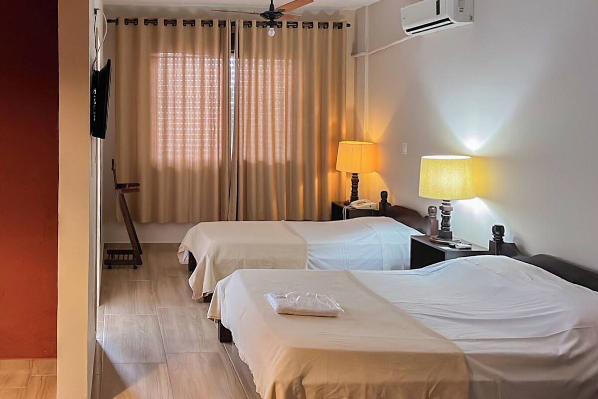 A hotel room with two beds, a desk with a lamp, a TV, and a window with curtains.
