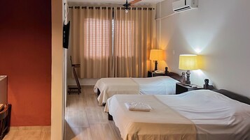 Habitación de hotel con dos camas, un escritorio con lámpara, televisión y ventana con cortinas.