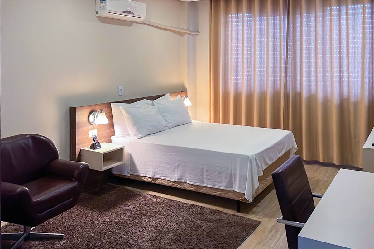 A hotel room with a bed, bedside table, lamp, and a TV on a stand.