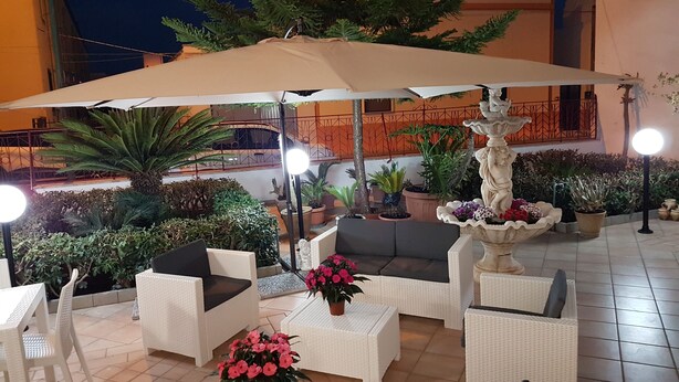 Un espace extérieur aménagé avec des meubles en osier blanc, un grand parasol et des plantes en pot.