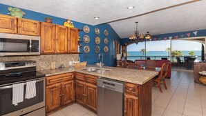 A kitchen with wooden cabinets, granite countertops, and a dishwasher. There is a view of the ocean through a large window.