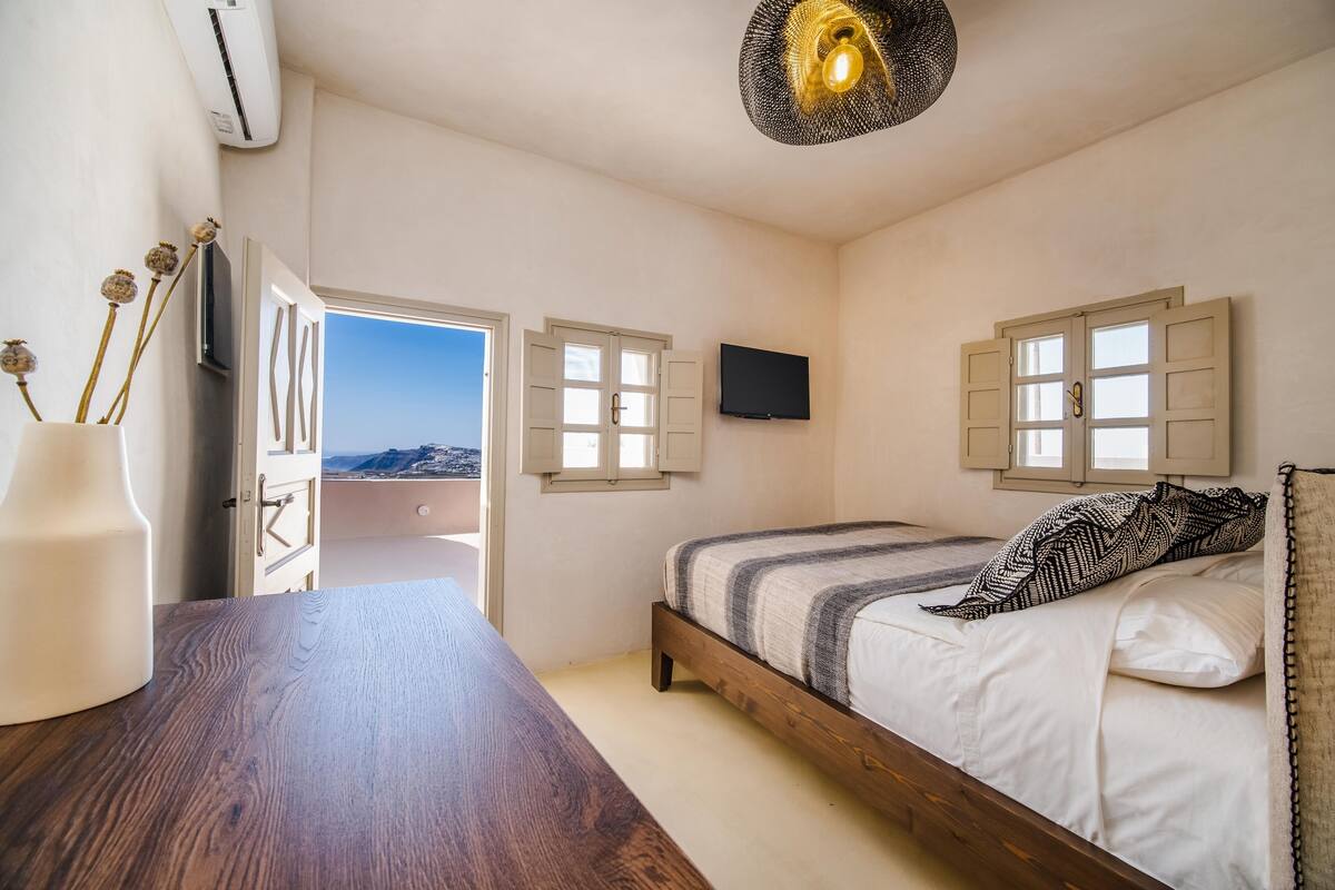 Une chambre à coucher avec un lit en bois, une table de chevet, un téléviseur fixé au mur et une fenêtre avec des volets.