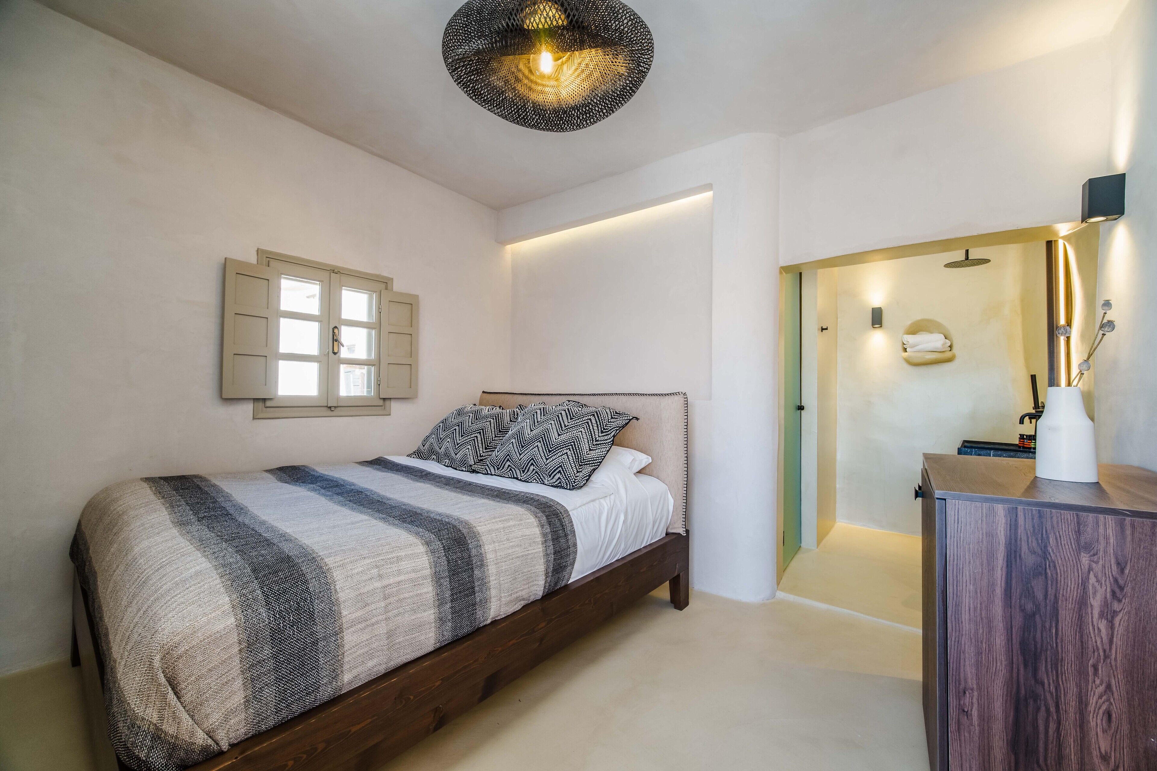 A bedroom with a bed, a bedside table, a wall-mounted light fixture, and a door leading to a bathroom.