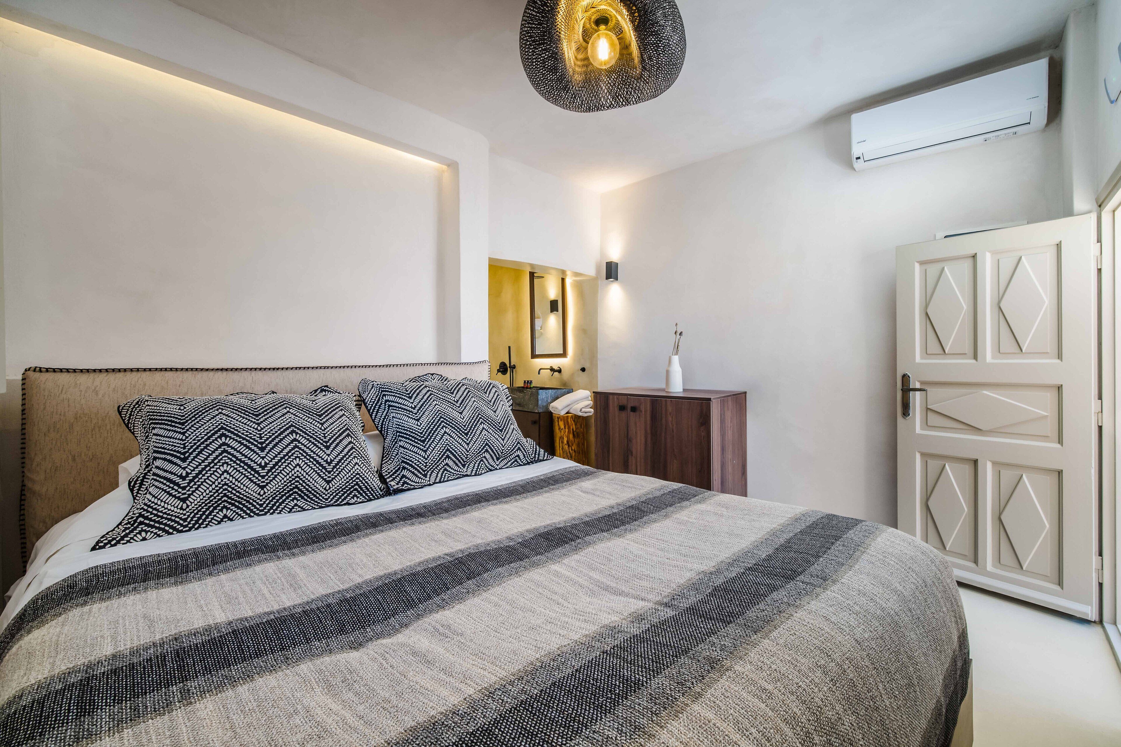 A bedroom with a large bed, a bedside table, a mirror, and a wardrobe.