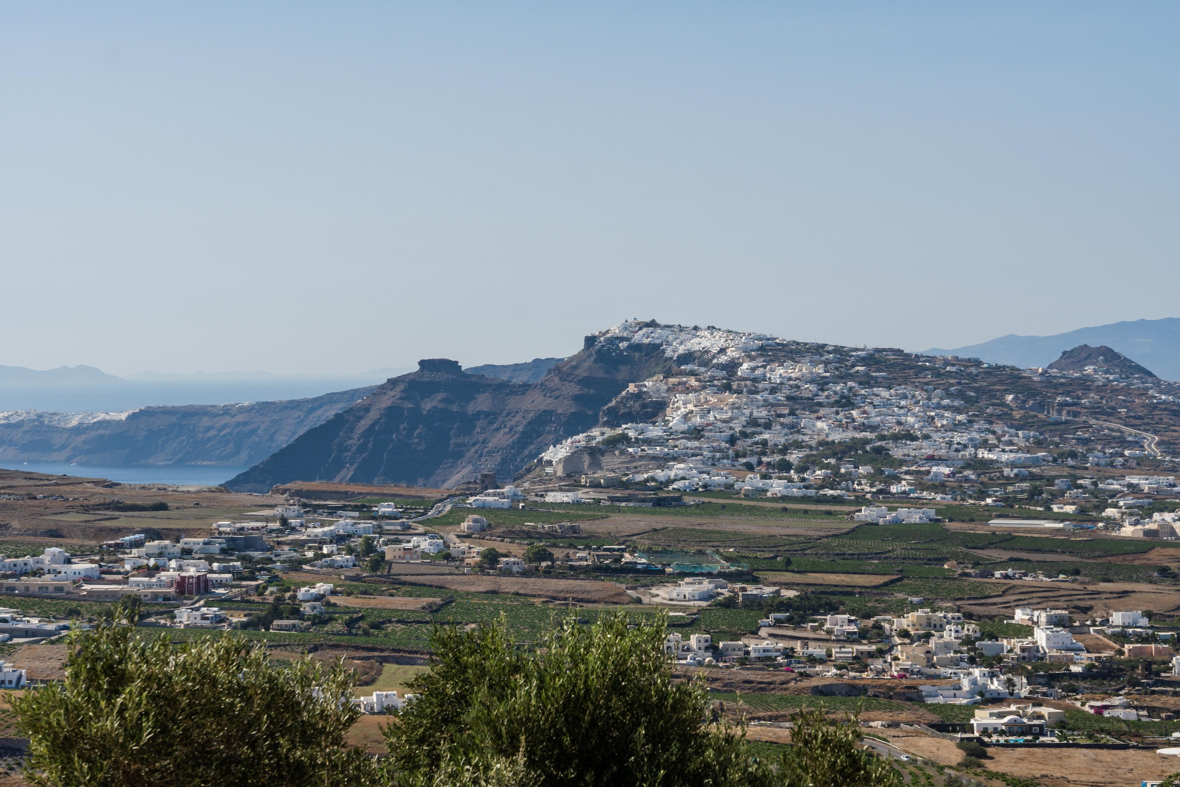 A coastal town with white buildings on a hillside, a prominent hilltop structure, and a view of the sea.