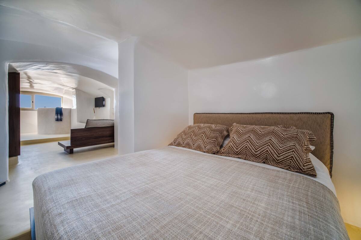 Une chambre avec un grand lit, une tête de lit en bois et une vue sur un balcon.
