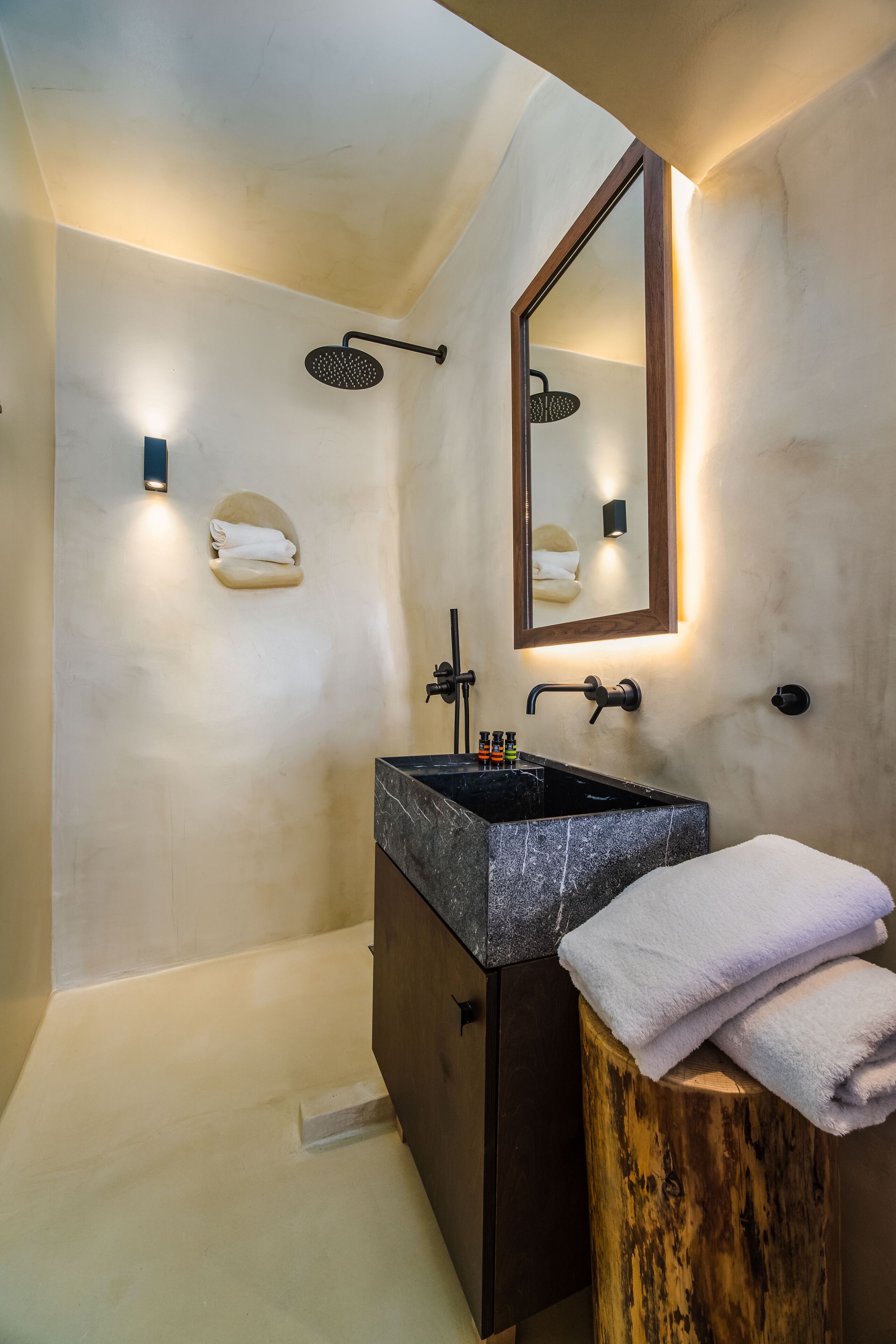 Un baño moderno con un lavamanos grande, un taburete de madera, un perchero para toallas y una ducha con cabezal de ducha manual.