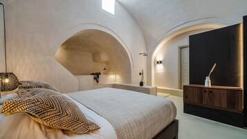 A bedroom with a large bed, a built-in bench, a vanity with a mirror, and a small skylight.