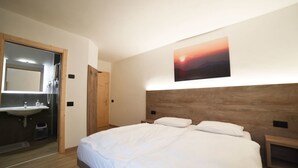 Une chambre à coucher avec une tête de lit en bois, un grand lit avec une literie blanche, une table de chevet et un tableau représentant un coucher de soleil, accroché au mur.