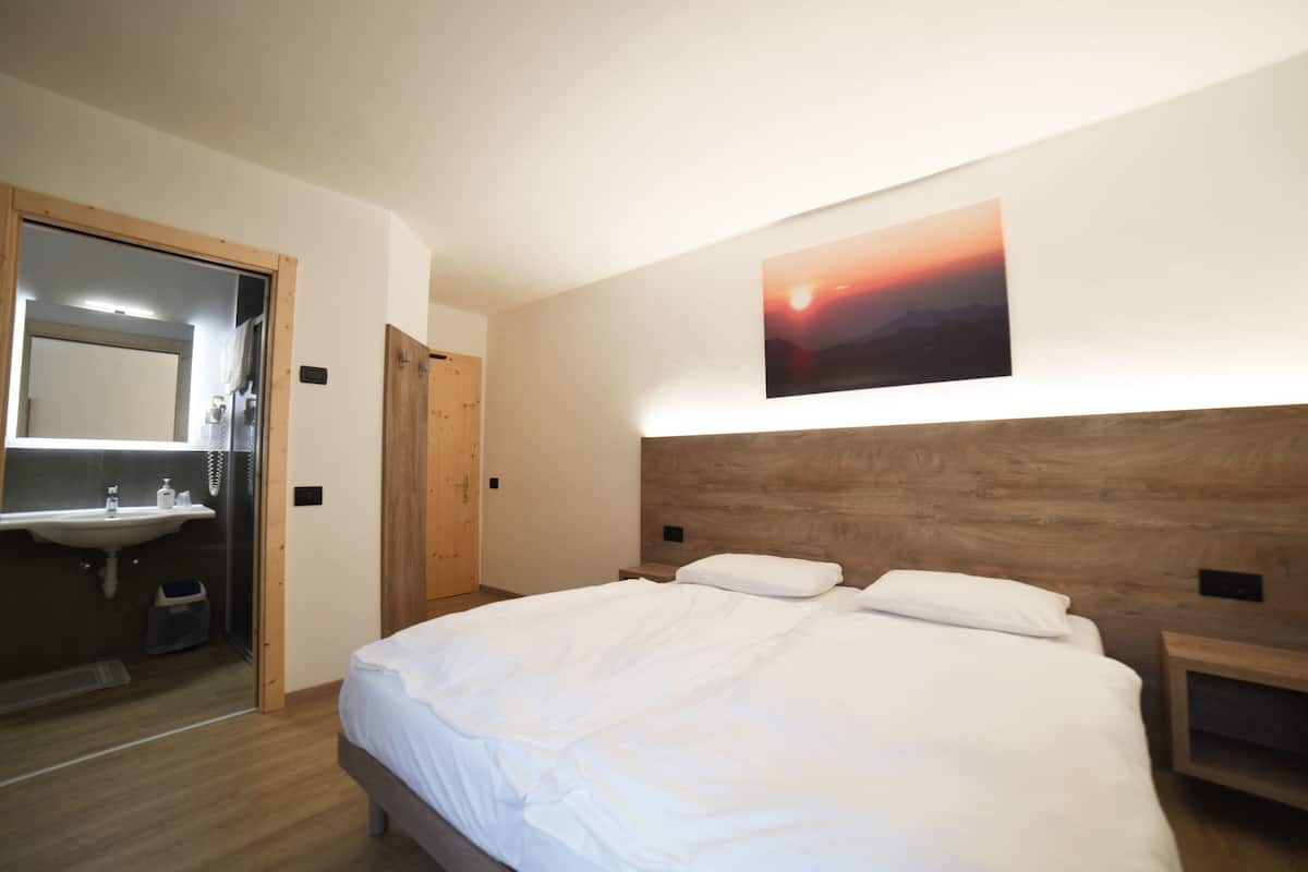 A bedroom with a wooden headboard, a large bed with white bedding, a nightstand, and a wall-mounted painting of a sunset.