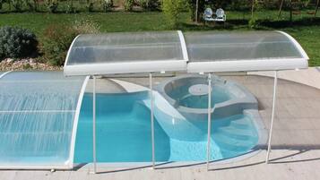 A covered outdoor swimming pool with a table and chairs in front.
