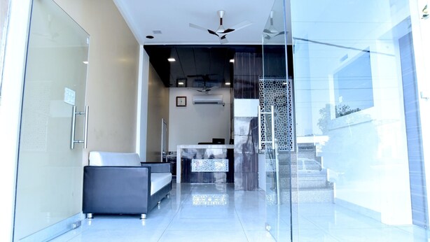 A modern hotel lobby with a reception desk, seating area, and a staircase leading to upper floors. - Hotel Metro View (Jaipur)
