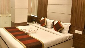 A bedroom with a bed, a bedside table, a nightstand, a ceiling fan, and a window with curtains. - Hotel Metro View (Jaipur)