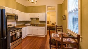 A compact kitchen with white cabinets, a stove, a microwave, and a dining area with a table and chairs. - Classic Uptown Shotgun, Just Steps to the Streetcar ! (New Orleans)