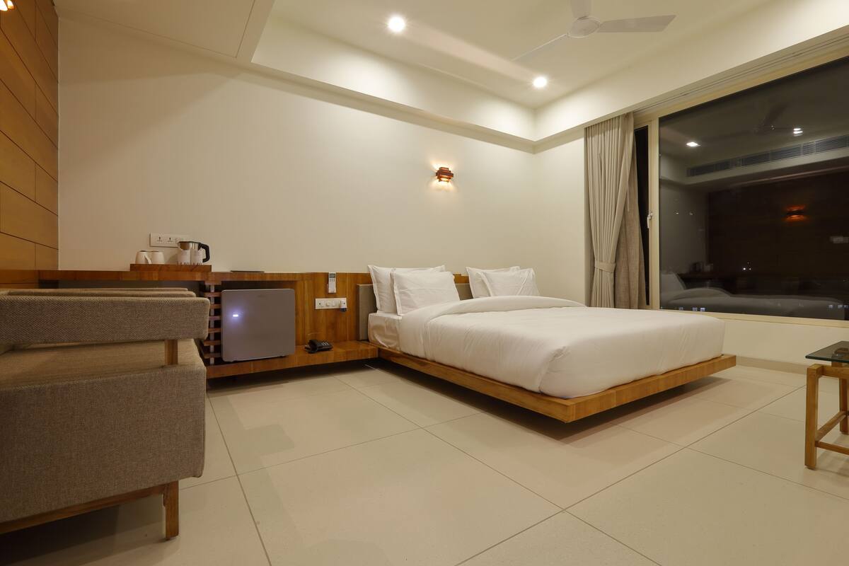 Una habitación de hotel moderna con cama, zona de estar, una mesita y una ventana con cortinas.
