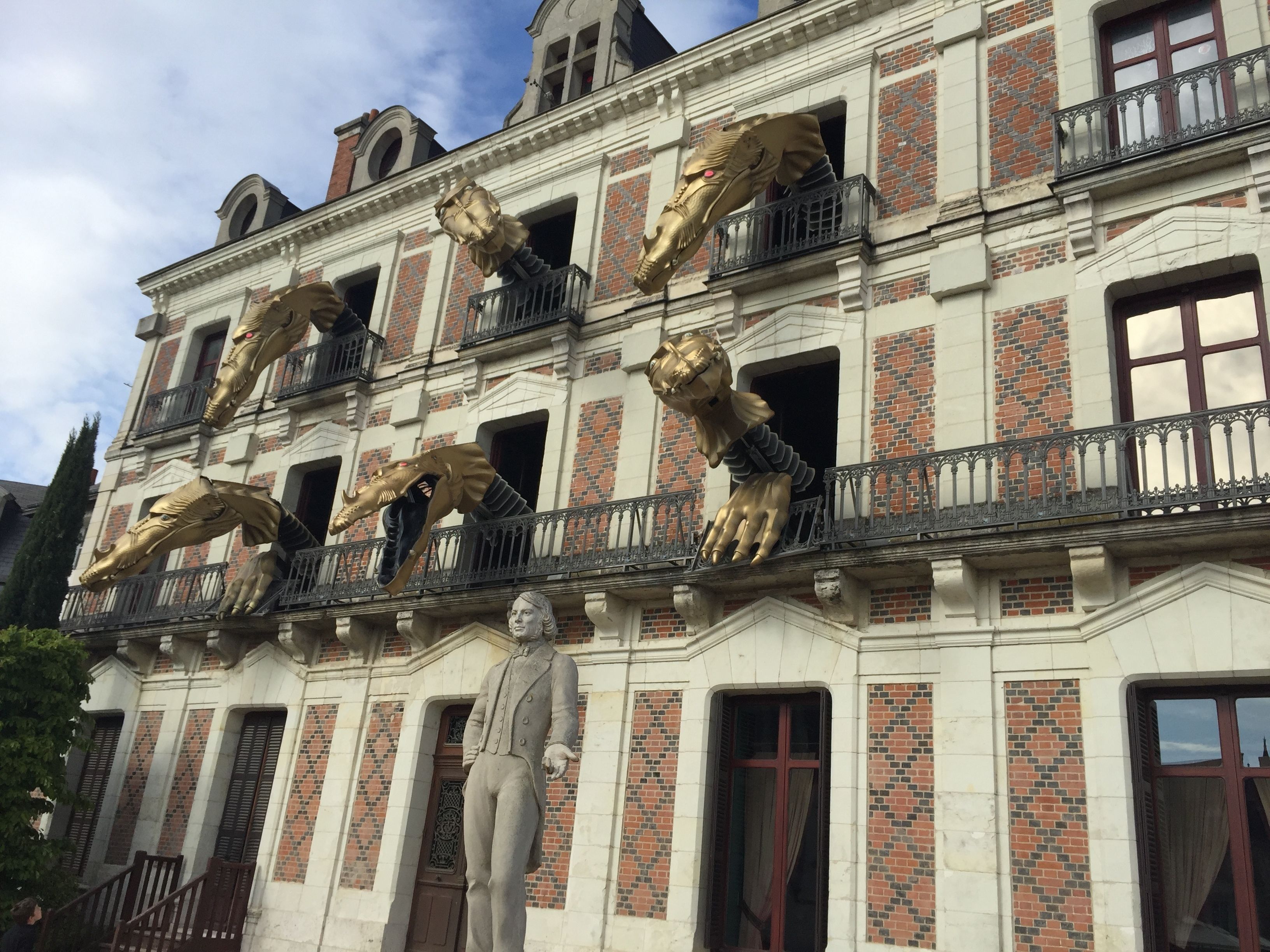 Een gebouw in klassieke stijl, met een opvallende standbeeld en decoratieve gouden leeuwen op de balkons.