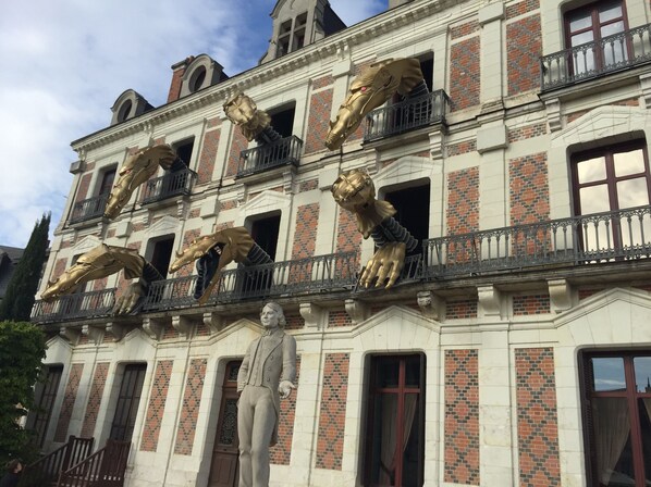 A building with a classical architectural style, featuring a prominent statue and decorative golden lion sculptures on the balconies.