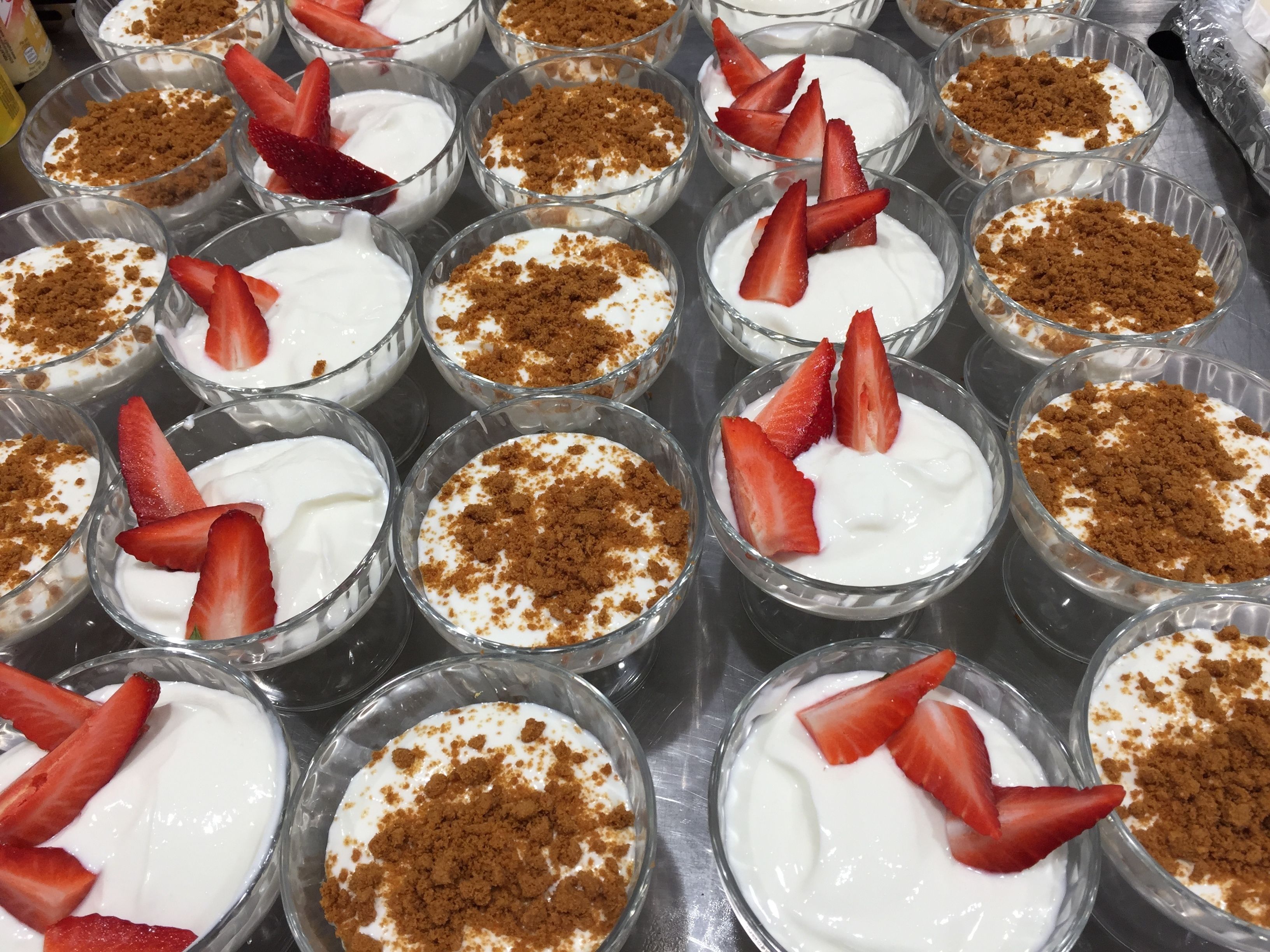 A tray of dessert cups with white cream and strawberries, topped with crumbled brown topping.