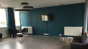 Une chambre moderne avec des murs de couleur turquoise, un téléviseur à écran plat fixé au mur, un tableau blanc et un coin salon avec des chaises et une petite table.