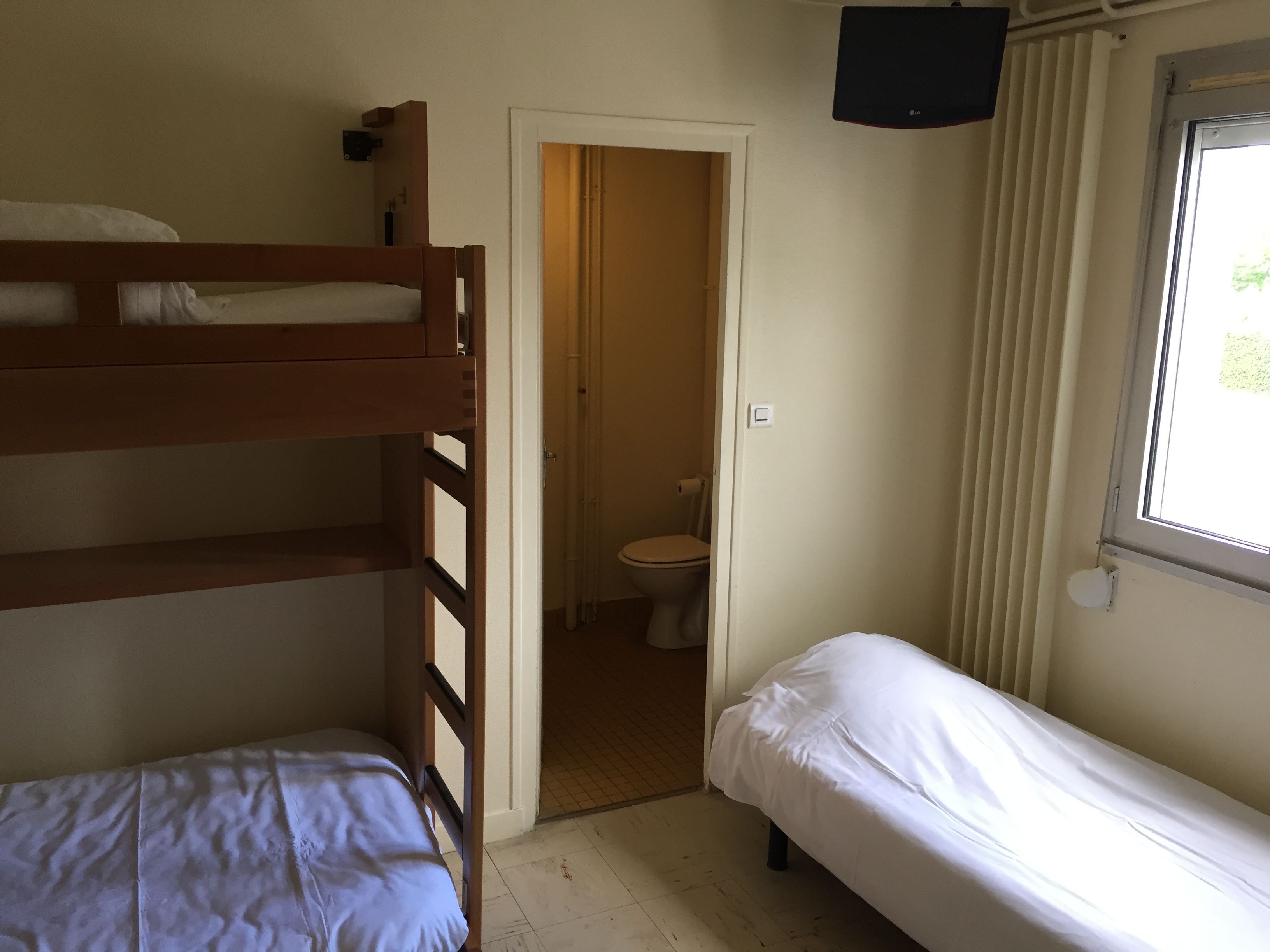 Una habitación con literas, una cama individual, un inodoro y una ventana con persianas.