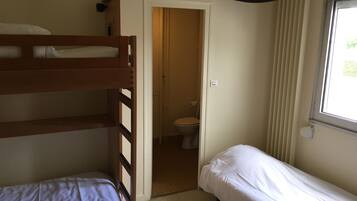 Ein Zimmer mit Etagenbett, einem Einzelbett, einer Toilette und einem Fenster mit Jalousien.