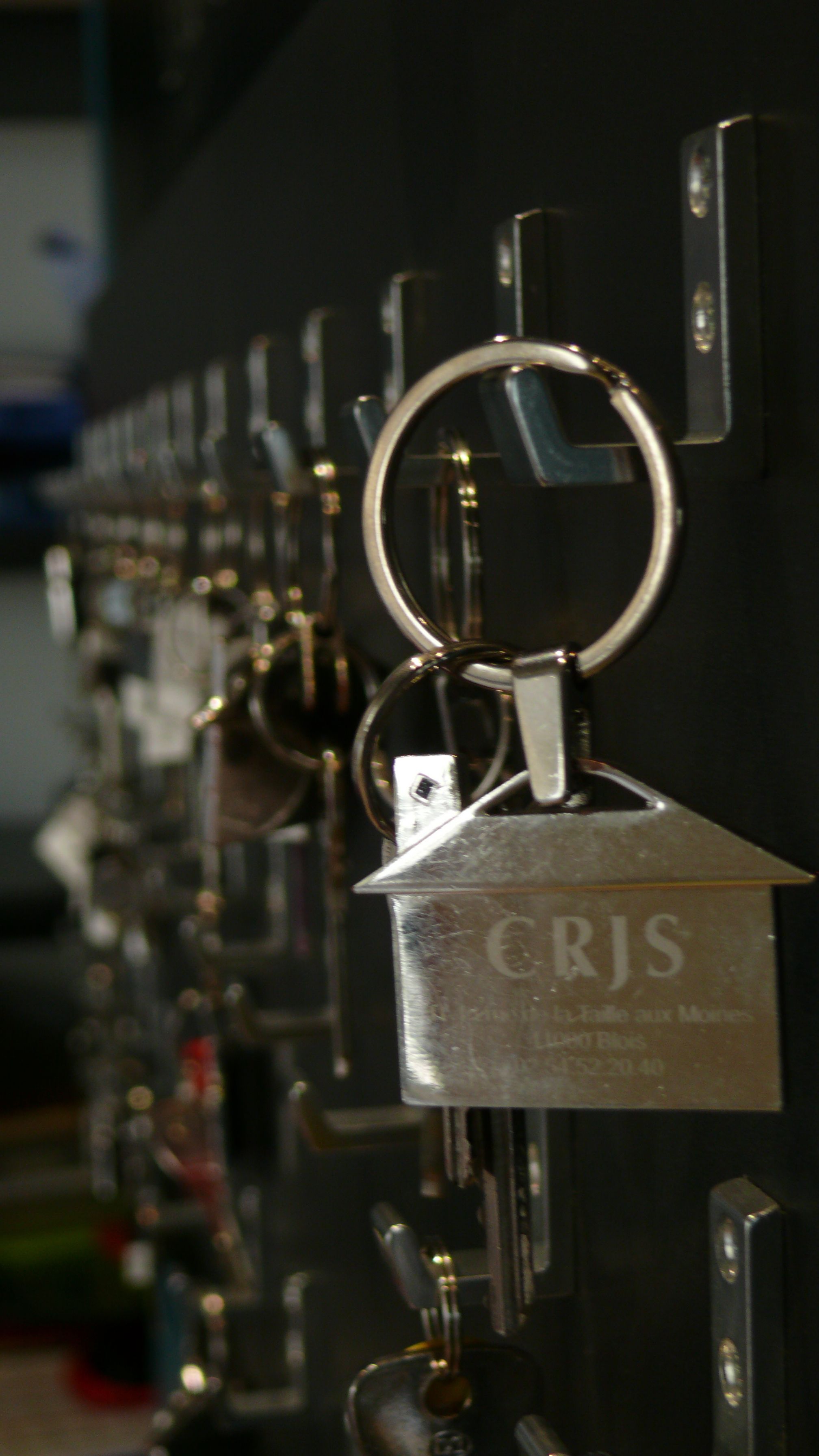 A row of keys hanging on a wall, each with a metal plate attached.