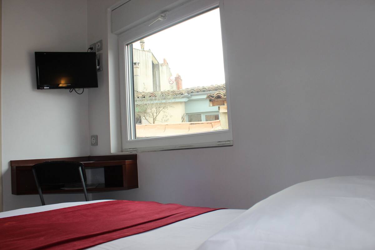 Habitación de hotel con una cama, un televisor fijado a la pared y una ventana con vistas a edificios.