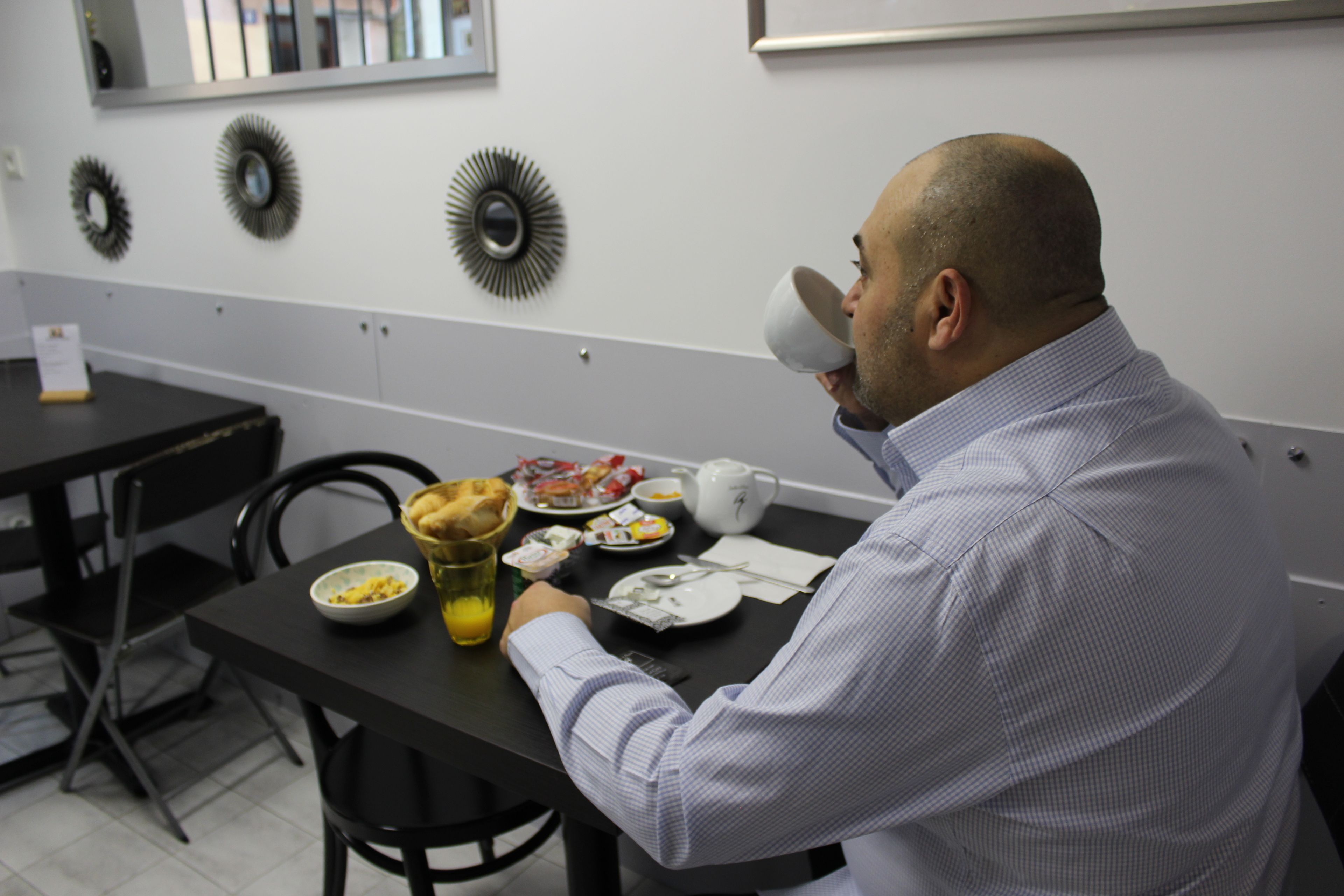 A man sitting at a table with breakfast items, including a bowl of cereal, a cup, and a plate with cutlery.