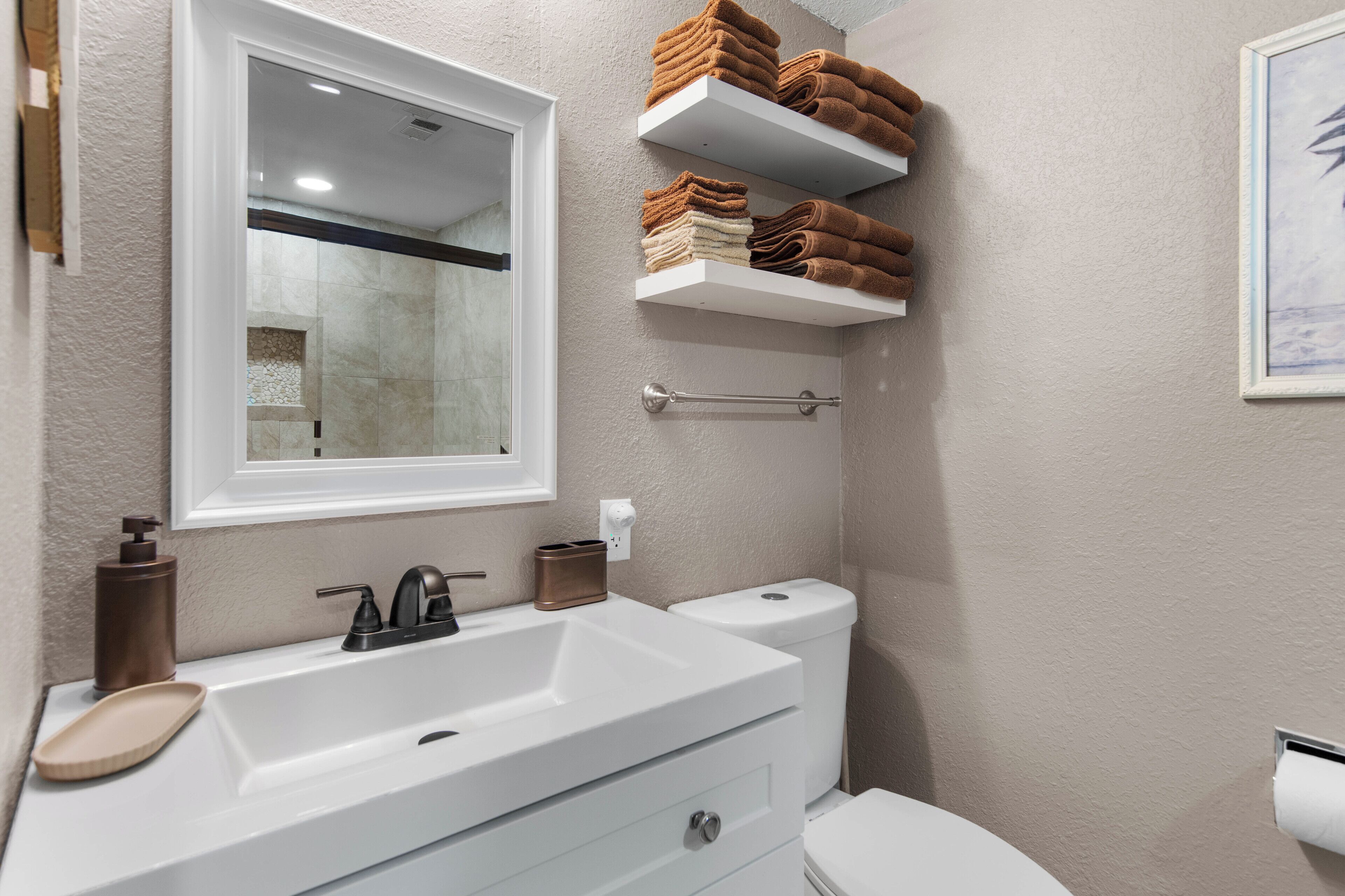 A bathroom with a white sink, a mirror, a toilet, and shelves with folded towels.