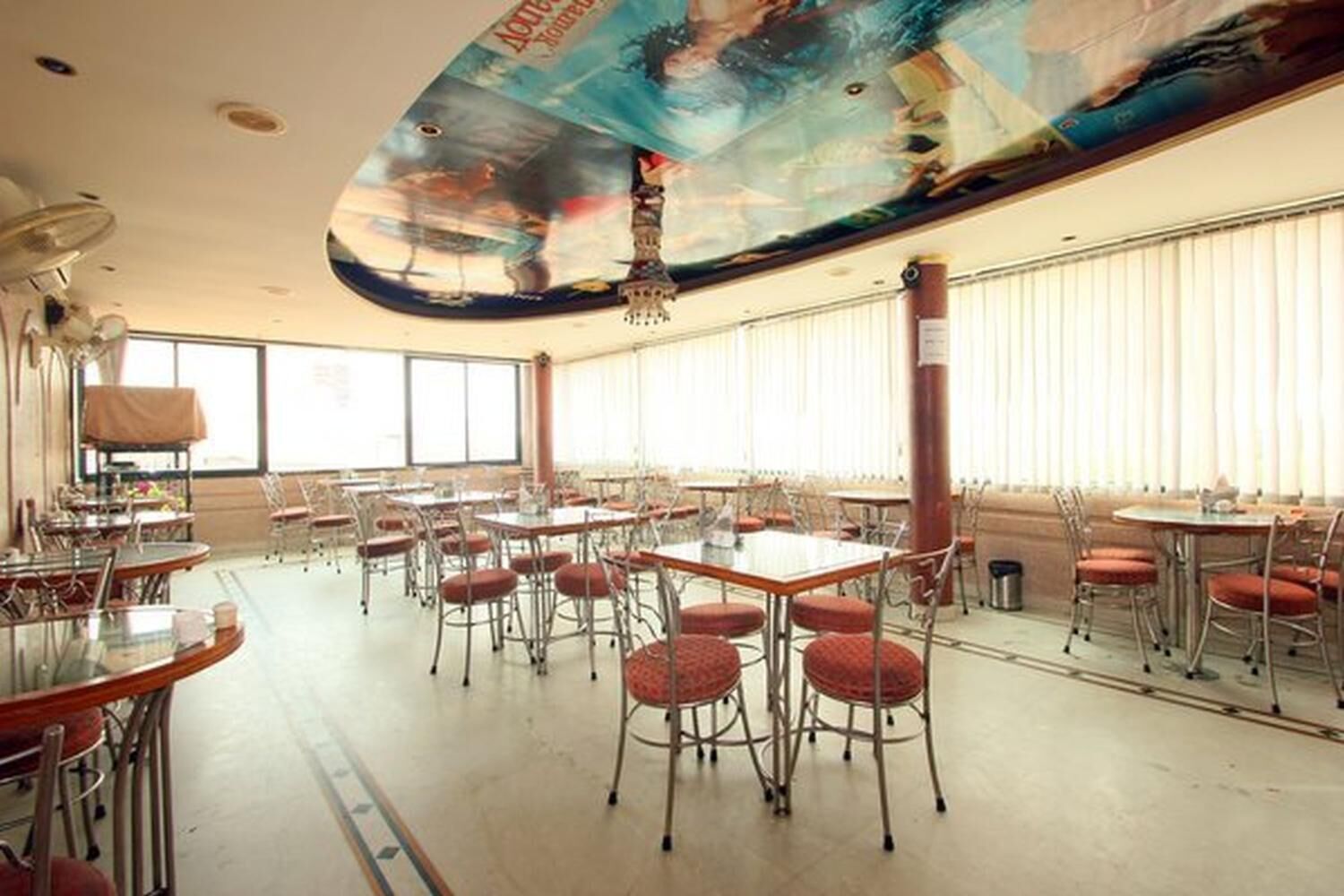 Uma ampla área de refeições com várias mesas e cadeiras, grandes janelas e um mural no teto.